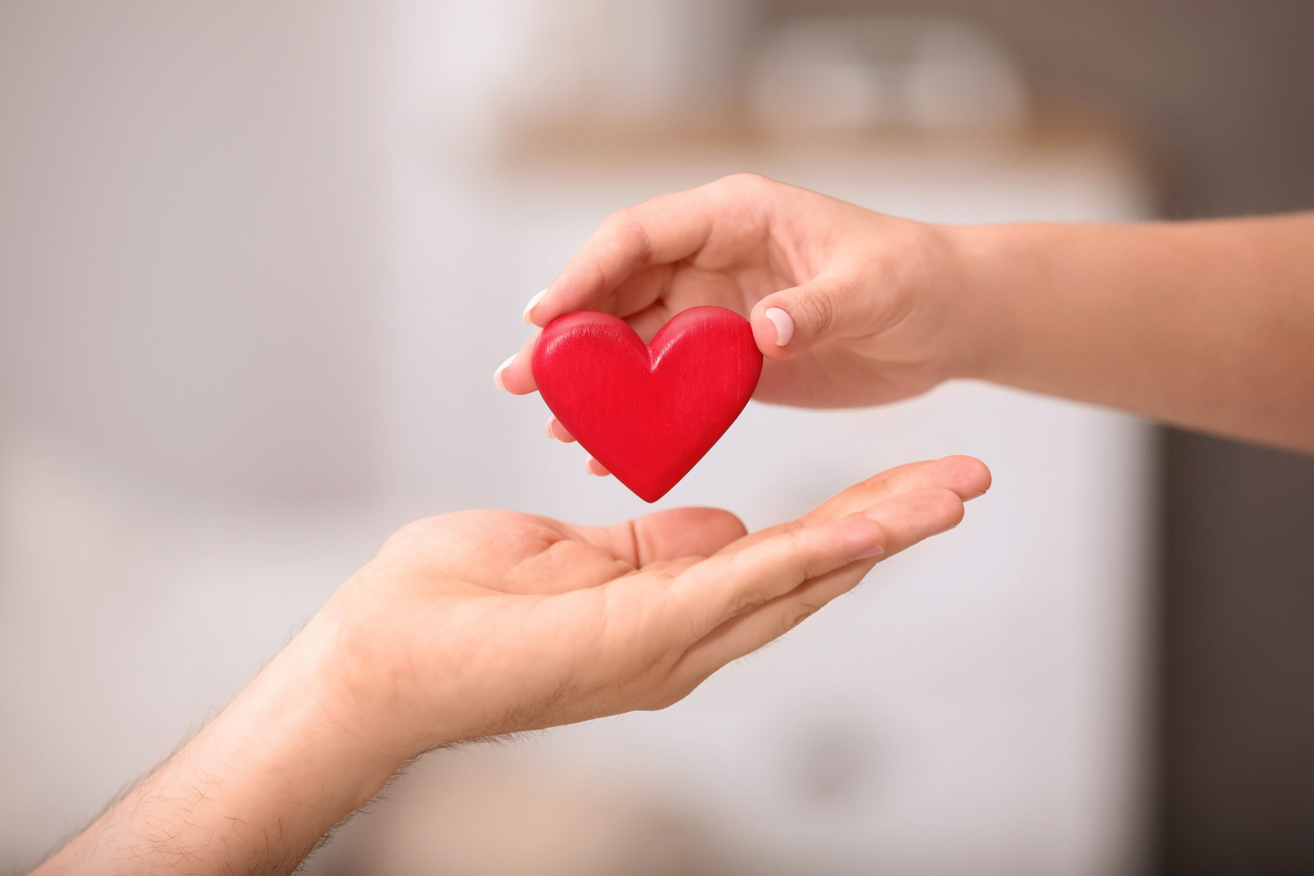Man giving red heart to woman on blurred background, closeup. Donation concept